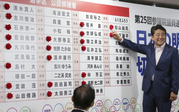 아베 신조 일본 총리가 21일 일본 도쿄 자민당 선거상황실에서 참의원 선거에서 승리한 여당 후보 당선자의 이름 옆에 당선 축하 표시 장식을 달고 있다.ⓒ뉴시스
