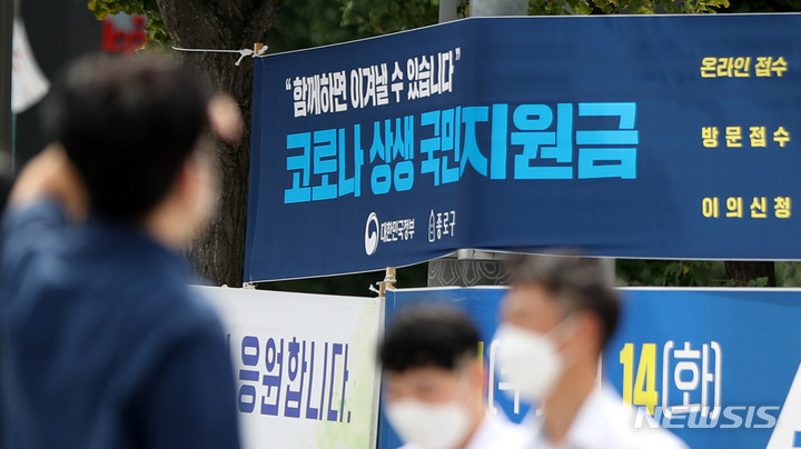 코로나19 상생 국민 지원금 신청이 시작된 6일 오전 서울 중로구 도심에서 시민들이 신청 안내 현수막 앞을 지나고 있다.